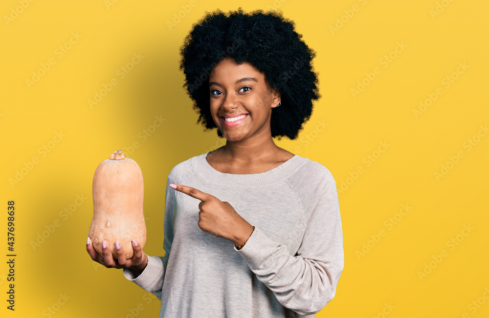 Young african american woman holding healthy fresh pumpkin smiling happy pointing with hand and finger Young african american woman holding healthy fresh pumpkin smiling happy pointing with hand and finger