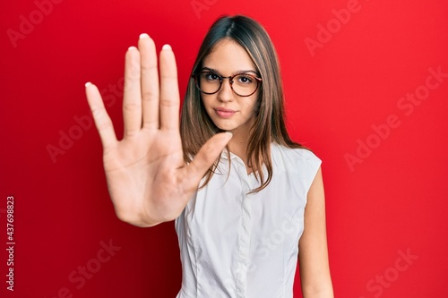 Young brunette woman wearing casual clothes and glasses doing stop sing with palm of the hand. warning expression with negative and serious gesture on the face. photo