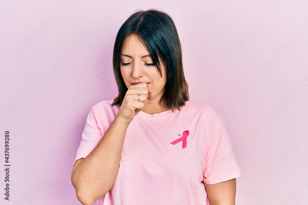 Young hispanic woman wearing pink cancer ribbon on t shirt feeling unwell and coughing as symptom for cold or bronchitis. health care concept. Young hispanic woman wearing pink cancer ribbon on t shirt feeling unwell and coughing as symptom for cold or bronchitis. health care concept.