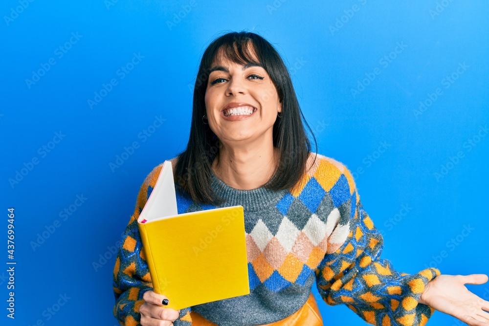 Obraz premium Young hispanic woman reading book celebrating victory with happy smile and winner expression with raised hands