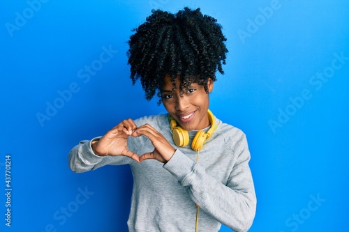 African american woman with afro hair wearing sweatshirt and using headphones smiling in love showing heart symbol and shape with hands. romantic concept.