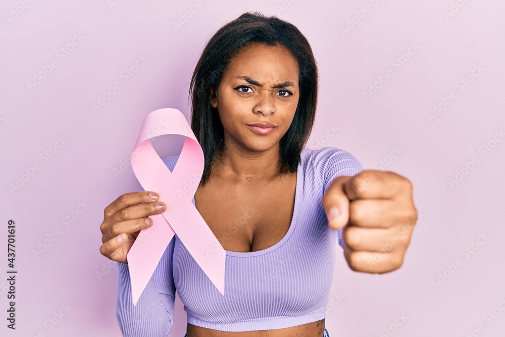 Young african american girl holding pink cancer ribbon annoyed and frustrated shouting with anger, yelling crazy with anger and hand raised Young african american girl holding pink cancer ribbon annoyed and frustrated shouting with anger, yelling crazy with anger and hand raised