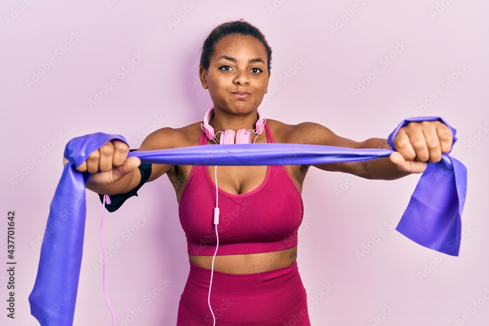 Young african american girl training arm resistance with elastic arm bands puffing cheeks with funny face. mouth inflated with air, catching air. Young african american girl training arm resistance with elastic arm bands puffing cheeks with funny face. mouth inflated with air, catching air.