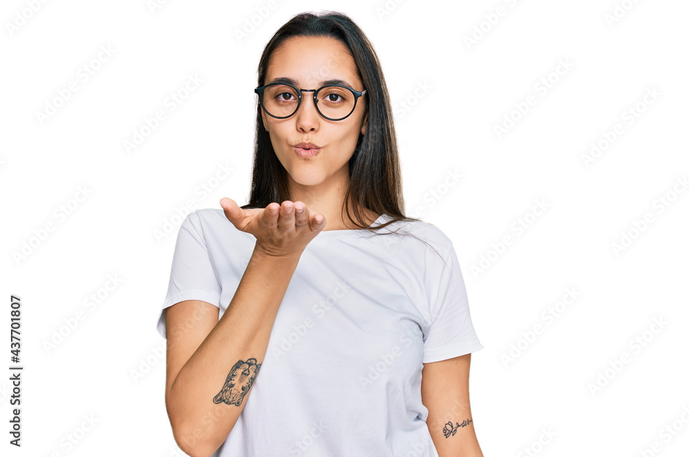Young hispanic woman wearing casual white t shirt looking at the camera blowing a kiss with hand on air being lovely and sexy. love expression. Young hispanic woman wearing casual white t shirt looking at the camera blowing a kiss with hand on air being lovely and sexy. love expression.