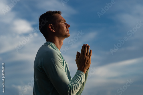 Young Man pray on blue sky background. Religion, faith and hope concept 
