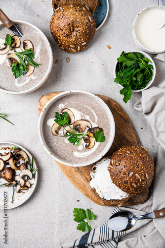 Traditional French mushroom cream soup with sour cream and parsley and rye bun on wooden board on natural linen background .