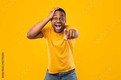 Excited African Guy Pointing Finger At Camera Laughing, Yellow Background