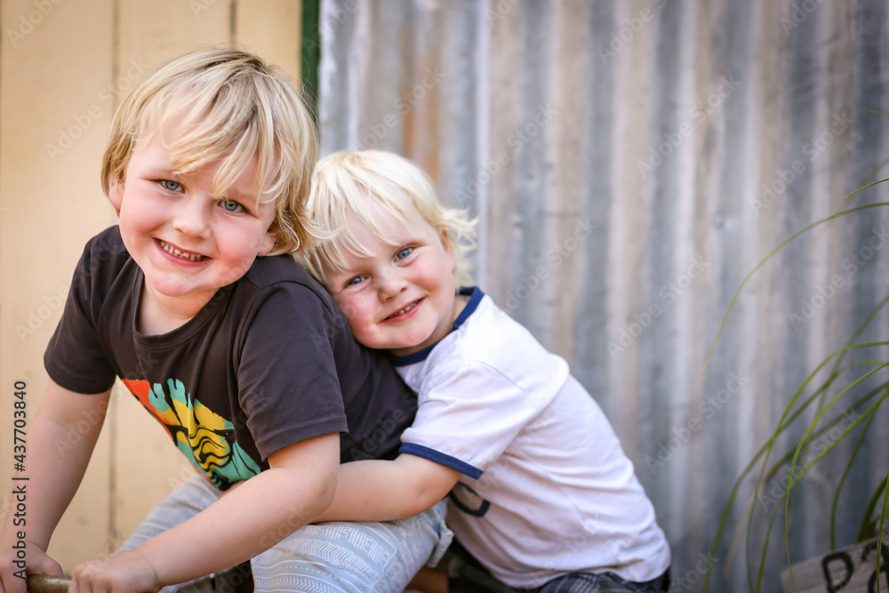 Two cute little caucasian boys playing happily together in front of tin shed in Australian country backyard Two cute little caucasian boys playing happily together in front of tin shed in Australian country backyard