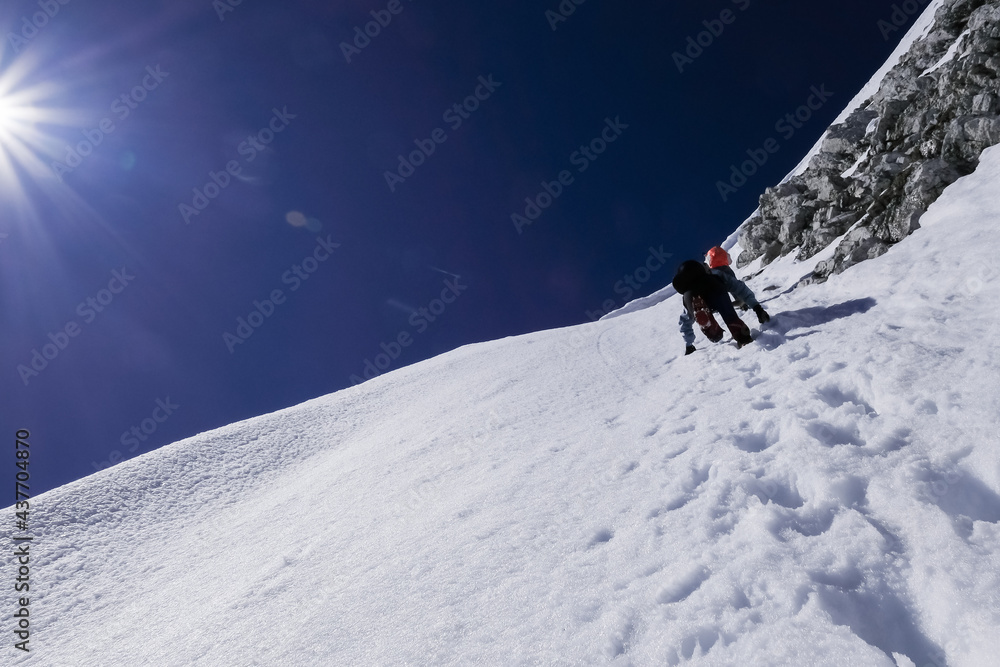 mountaineers with ice axes climb a sheer ice wall on a snowy alpine slope