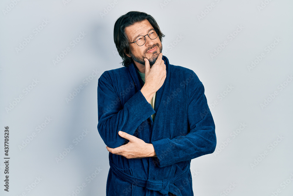 Middle age caucasian man wearing bathrobe and glasses with hand on chin thinking about question, pensive expression. smiling with thoughtful face. doubt concept. Middle age caucasian man wearing bathrobe and glasses with hand on chin thinking about question, pensive expression. smiling with thoughtful face. doubt concept.