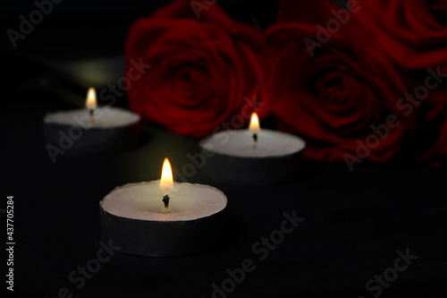 Mourning concept. Burning candles and flowers on a black mourning background