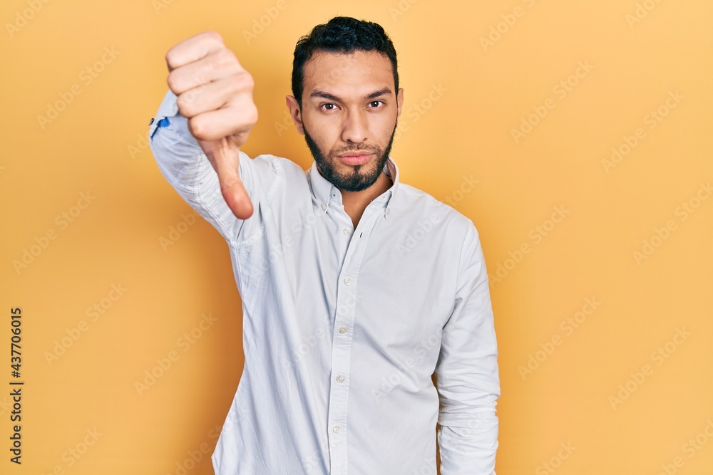 Hispanic man with beard wearing business shirt looking unhappy and angry showing rejection and negative with thumbs down gesture. bad expression. Hispanic man with beard wearing business shirt looking unhappy and angry showing rejection and negative with thumbs down gesture. bad expression.