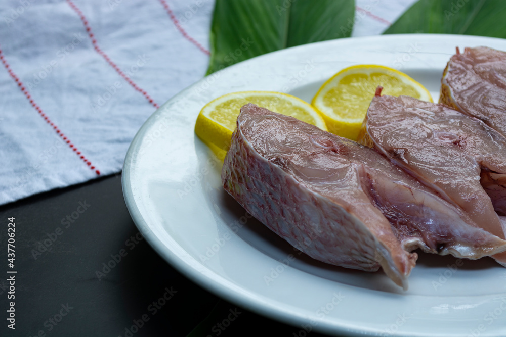 Fresh raw fish on white plate with green leaf and lemon