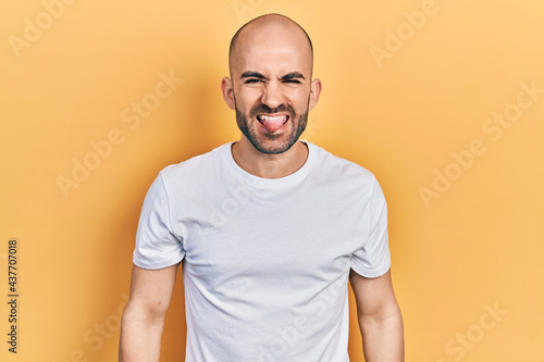 Young bald man wearing casual white t shirt sticking tongue out happy with funny expression. emotion concept.