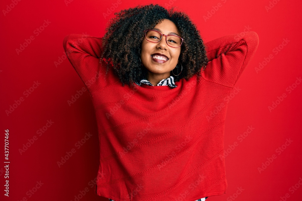 Beautiful african american woman with afro hair wearing sweater and glasses relaxing and stretching, arms and hands behind head and neck smiling happy Beautiful african american woman with afro hair wearing sweater and glasses relaxing and stretching, arms and hands behind head and neck smiling happy
