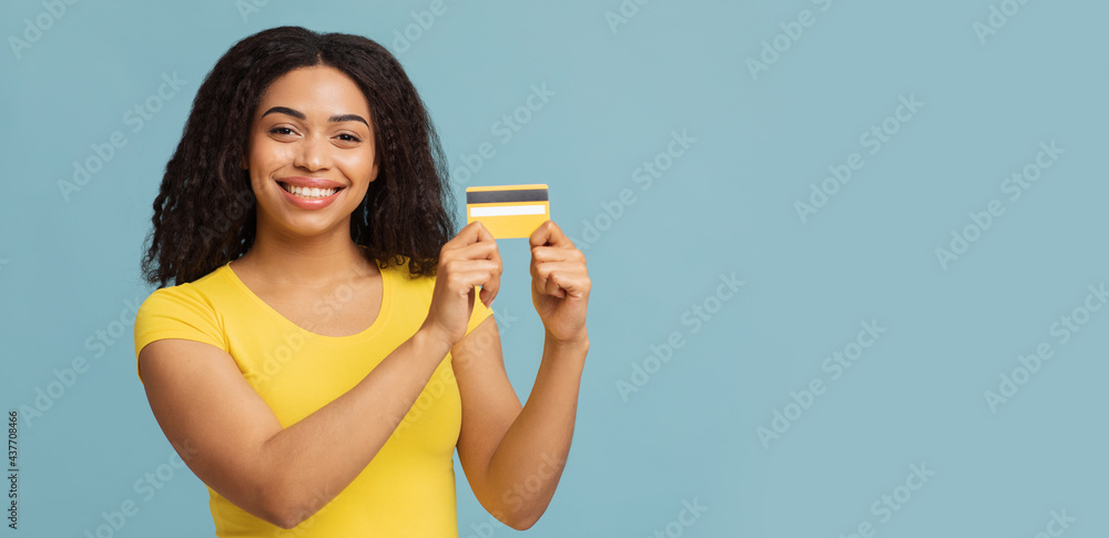 Easy payment concept. Happy african american lady holding credit card, looking and smiling to camera, blue background Easy payment concept. Happy african american lady holding credit card, looking and smiling to camera, blue background
