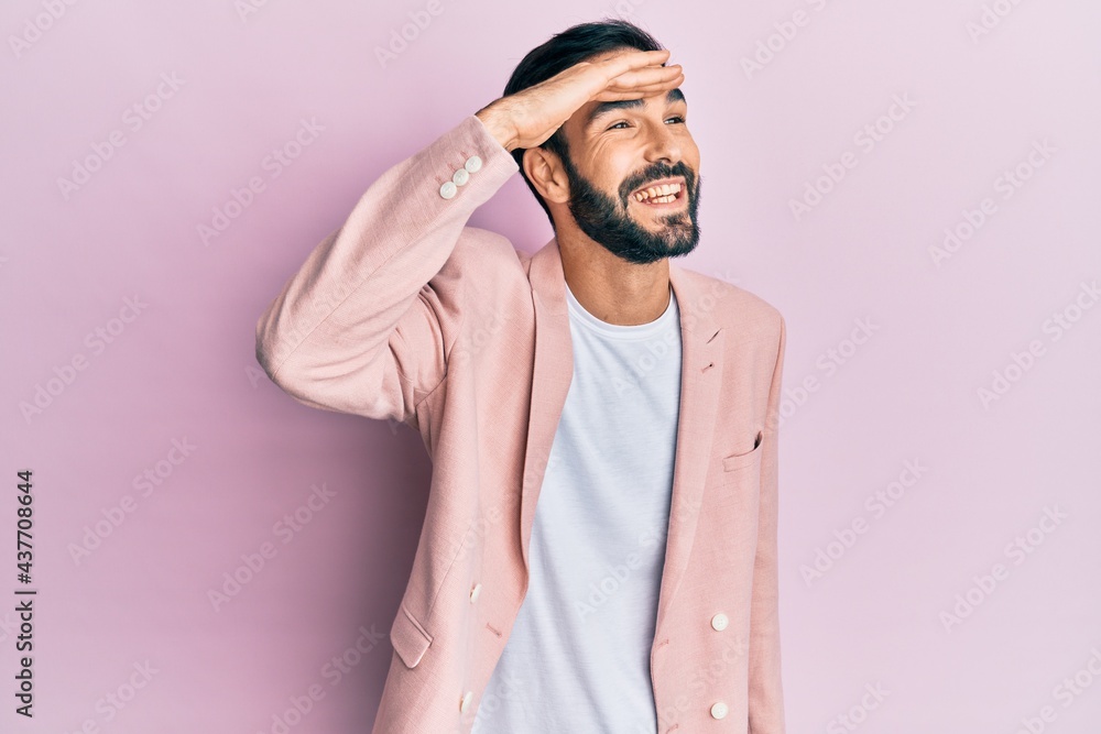 Young hispanic man wearing business jacket very happy and smiling looking far away with hand over head. searching concept.