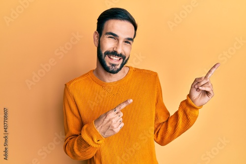 Young hispanic man wearing casual clothes smiling and looking at the camera pointing with two hands and fingers to the side. © Krakenimages.com