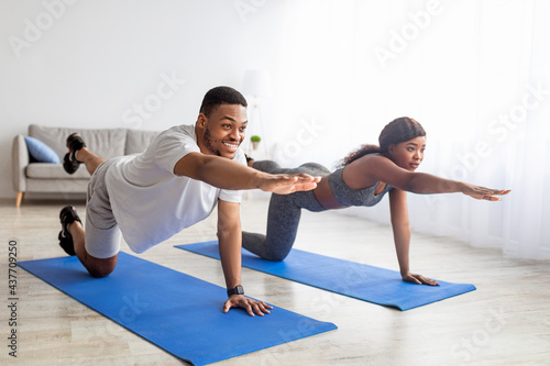 Fit black couple stretching their arms and legs, doing yoga or pilates on mat indoors. Stay home hobbies