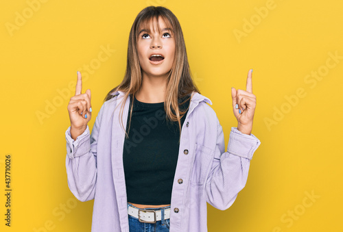 Teenager caucasian girl wearing casual clothes amazed and surprised looking up and pointing with fingers and raised arms.