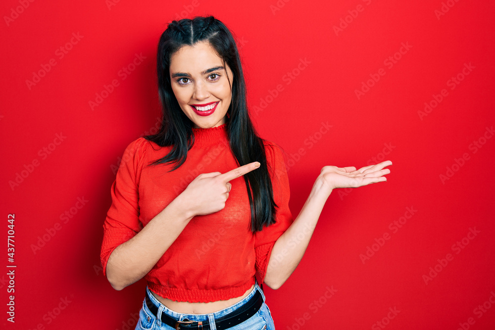 Young hispanic girl wearing casual clothes amazed and smiling to the camera while presenting with hand and pointing with finger. Young hispanic girl wearing casual clothes amazed and smiling to the camera while presenting with hand and pointing with finger.
