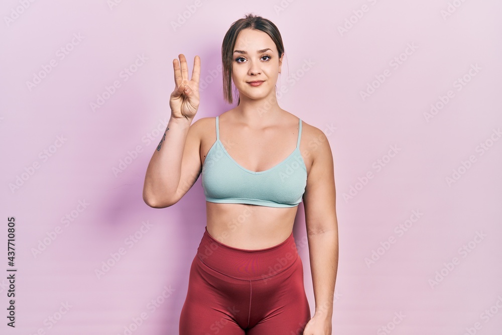 Young hispanic girl wearing sportswear showing and pointing up with fingers number three while smiling confident and happy.