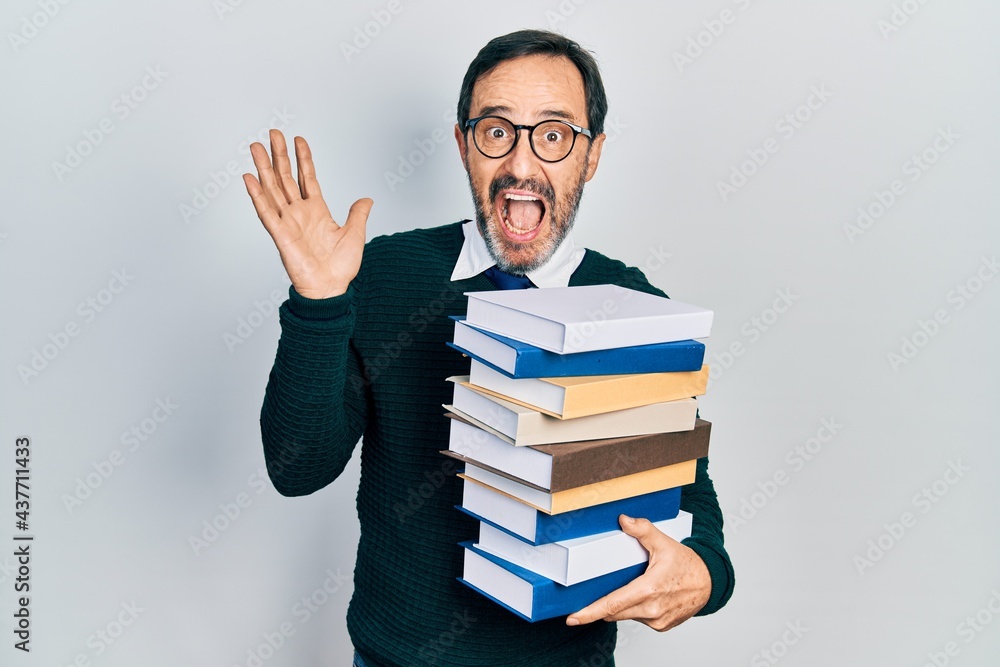 Middle age hispanic man holding a pile of books celebrating crazy and amazed for success with open eyes screaming excited. Middle age hispanic man holding a pile of books celebrating crazy and amazed for success with open eyes screaming excited.