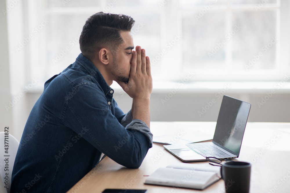Exhausted arab man sitting in front of laptop, office interior Exhausted arab man sitting in front of laptop, office interior