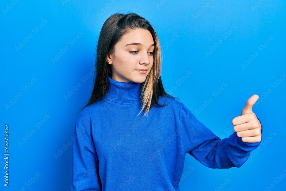 Young brunette girl wearing turtleneck sweater looking proud, smiling doing thumbs up gesture to the side Young brunette girl wearing turtleneck sweater looking proud, smiling doing thumbs up gesture to the side