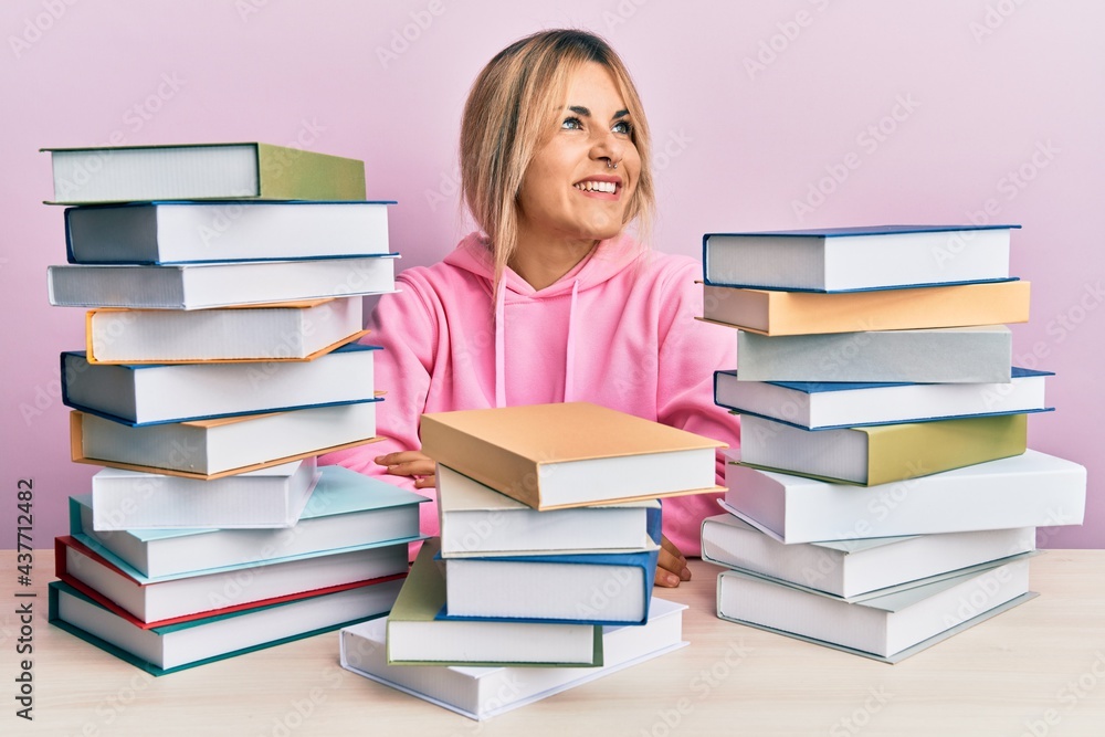 Young caucasian woman sitting on the table with books smiling looking to the side and staring away thinking. Young caucasian woman sitting on the table with books smiling looking to the side and staring away thinking.