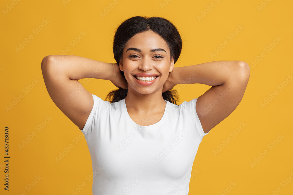 Happy young black woman touching and playing with her hair, looking and smiling to camera over yellow background Happy young black woman touching and playing with her hair, looking and smiling to camera over yellow background