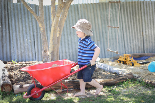 Fotografie, Obraz Little toddler boy pushing kid's wheelbarrow