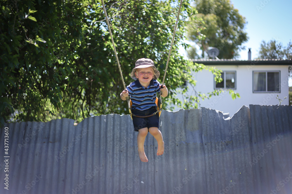 Happy little boy playing on backyard swing