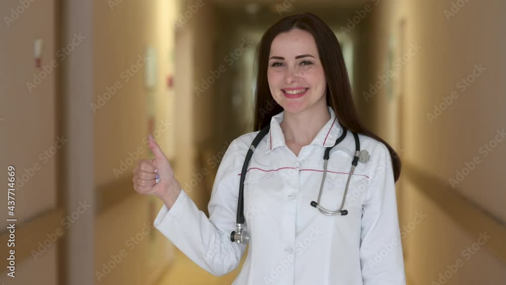 Friendly female doctor in medical Uniform standing in hospital corridor showing thumbs up. Health care and medical concept. Medical workers. Friendly female doctor in medical Uniform standing in hospital corridor showing thumbs up. Health care and medical concept. Medical workers.