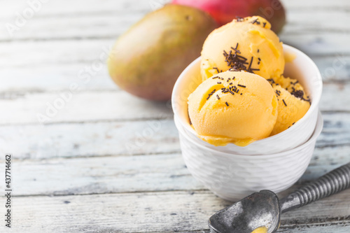 Homemade mango ice cream in a bowls with fresh fruits over white wooden background.