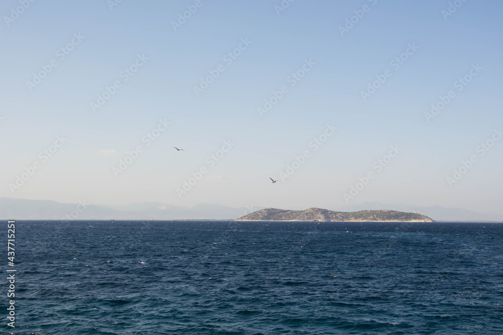Small distant land in the ocean, beautiful blue ocean and blue sky. Tranquil calm water, travel destination, summer landscape, birds flying