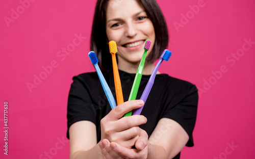 Beautiful happy young woman with different colored toothbrushes on blank pink background
