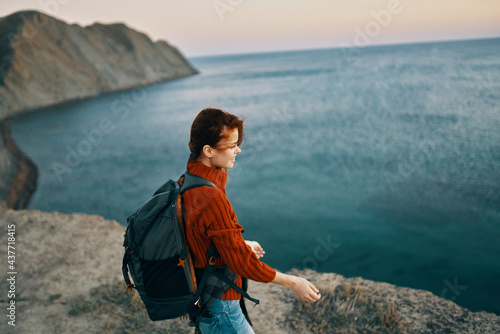 traveler in a red sweater and jeans with a backpack in the mountains near the sea top view