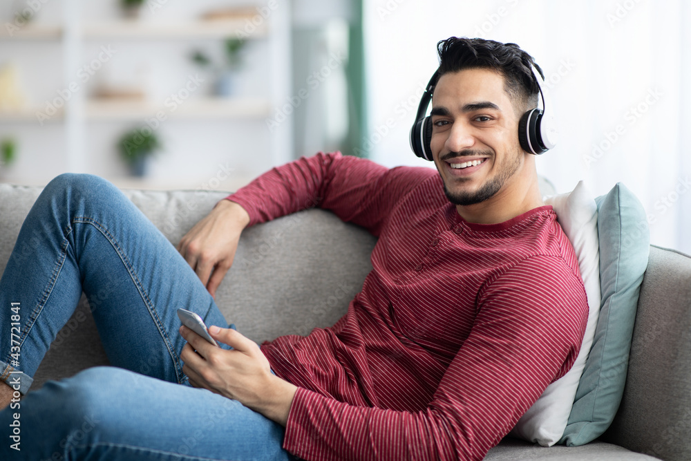 Obraz premium Cheerful arab guy listening to music, using mobile phone