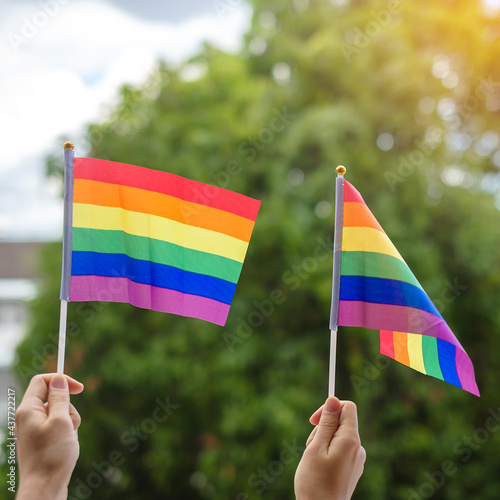 hands showing LGBTQ Rainbow flag on green nature background. Support Lesbian  Gay  Bisexual  Transgender and Queer community and Pride month concept