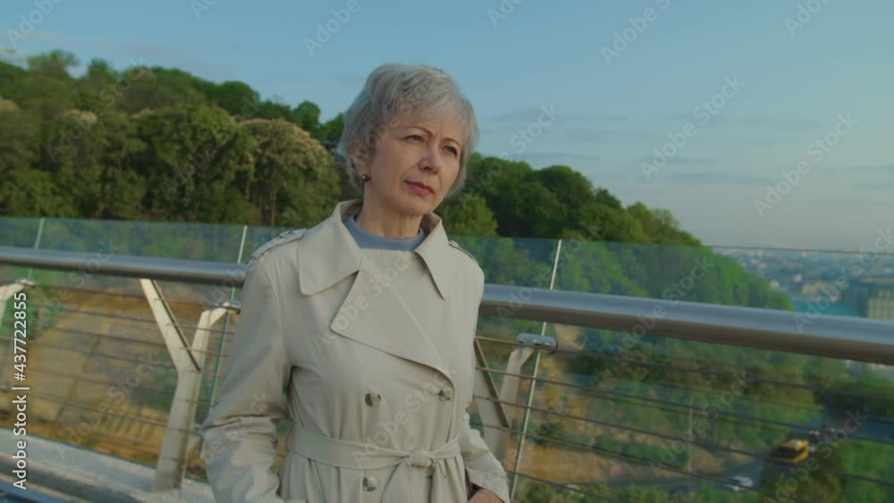 Senior woman in casual clothing standing in city park waiting for husband. Elderly bearded man approaching woman and presenting flowers. She expressing exitement and surprising to meet her spouse
