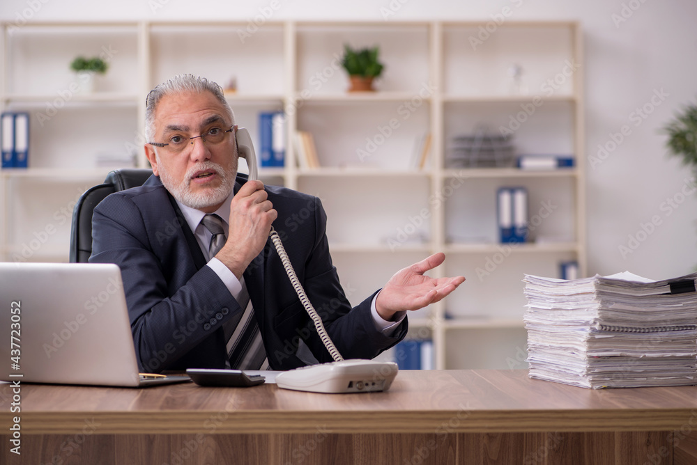 Aged male employee unhappy with excessive work in the office Aged male employee unhappy with excessive work in the office