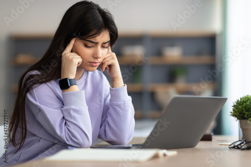 Tired woman massaging temples sitting at desk with laptop