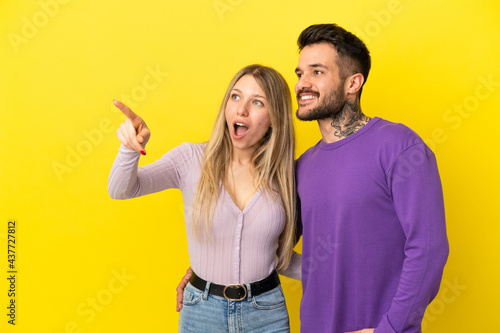 Young couple over isolated yellow background pointing finger to the side and presenting a product