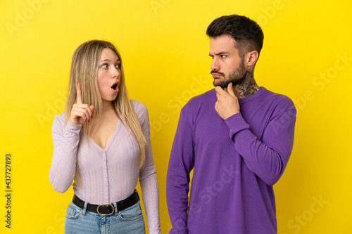 Young couple over isolated yellow background standing and thinking an idea