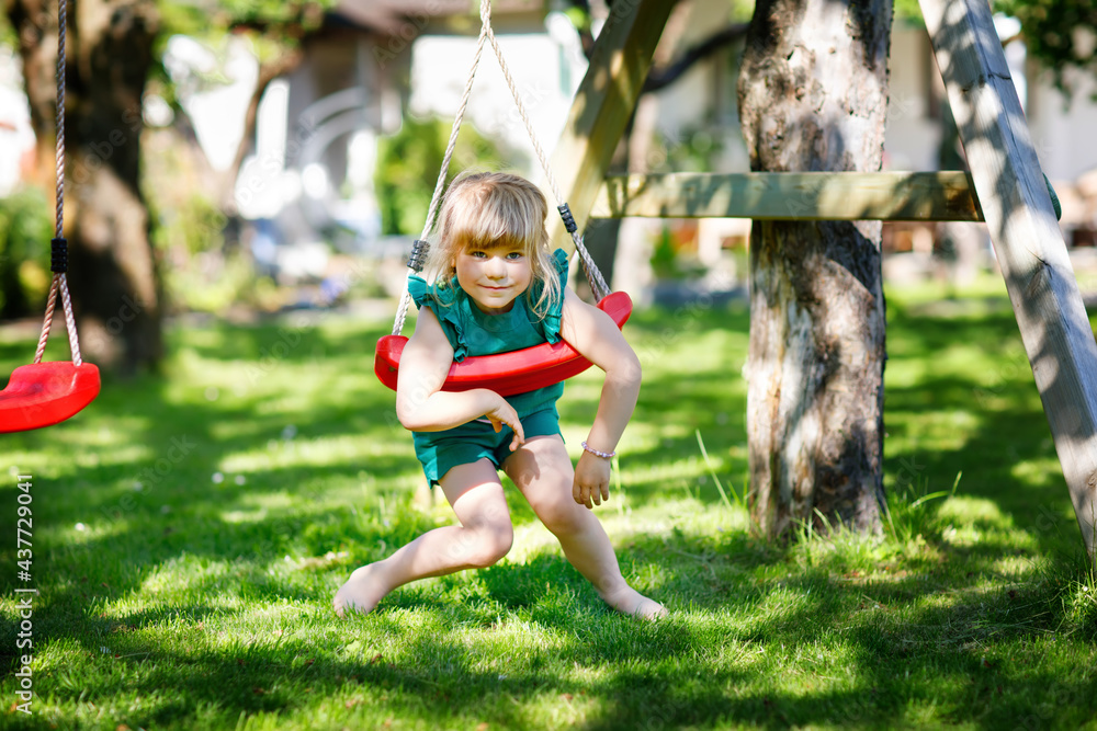 Happy little preschool girl having fun on swing in domestic garden. Healthy toddler child swinging on sunny summer day. Children activity outdoor, active smiling kid laughing