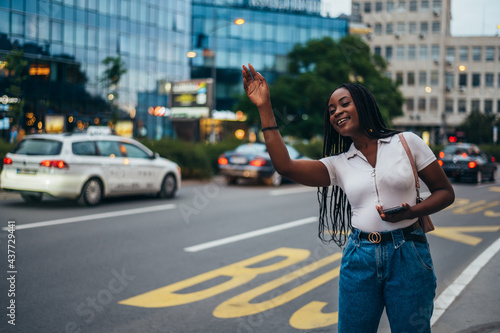 Cheerful african american woman calling for a cab and using a smartphone