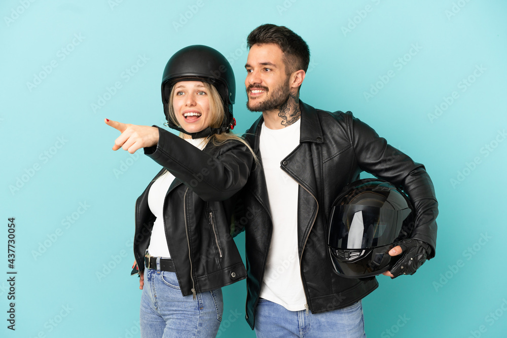 Couple with motorcycle helmet over isolated blue background pointing to the side to present a product Couple with motorcycle helmet over isolated blue background pointing to the side to present a product