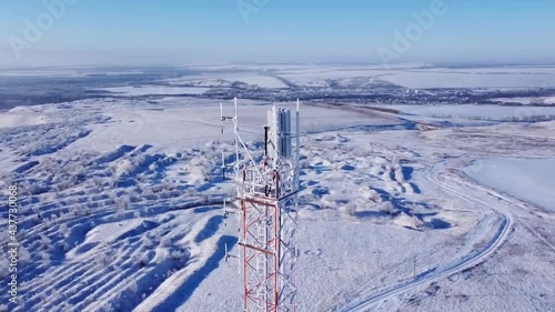 Winter. Telephone communication tower. TV repeater. Drone shooting. Blue sky. Sunny day. The tower is red and white. Tall construction, metal structure.