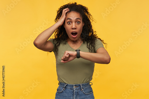 amazed and shocked african american female keeps her hand on head, starring into camera with stressed facial expression. She missed her bus. Isolated over yellow background